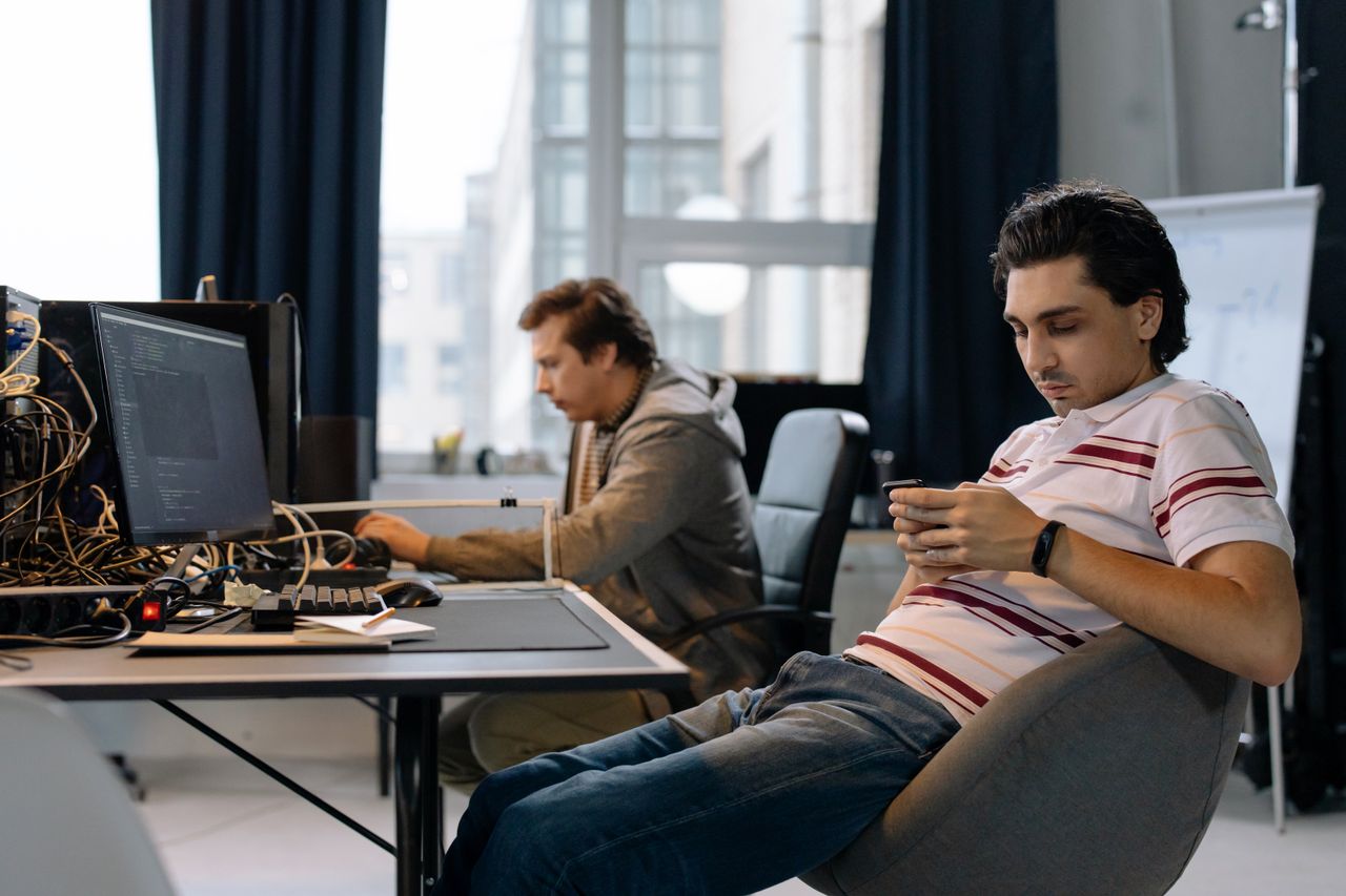 Services Two men working in a modern office, one on a computer and the other on a smartphone.